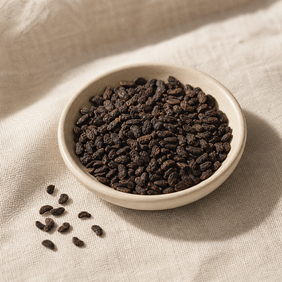 Dried babchi seeds in a ceramic dish on cream linen