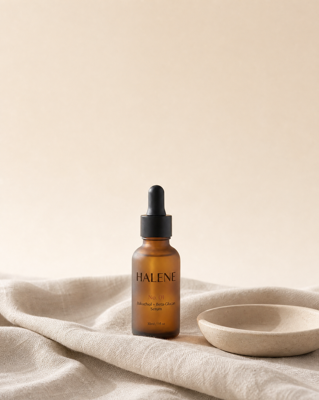 HALENE No. 01 Bakuchiol + Beta-Glucan Serum in frosted amber glass on natural linen beside a ceramic dish
